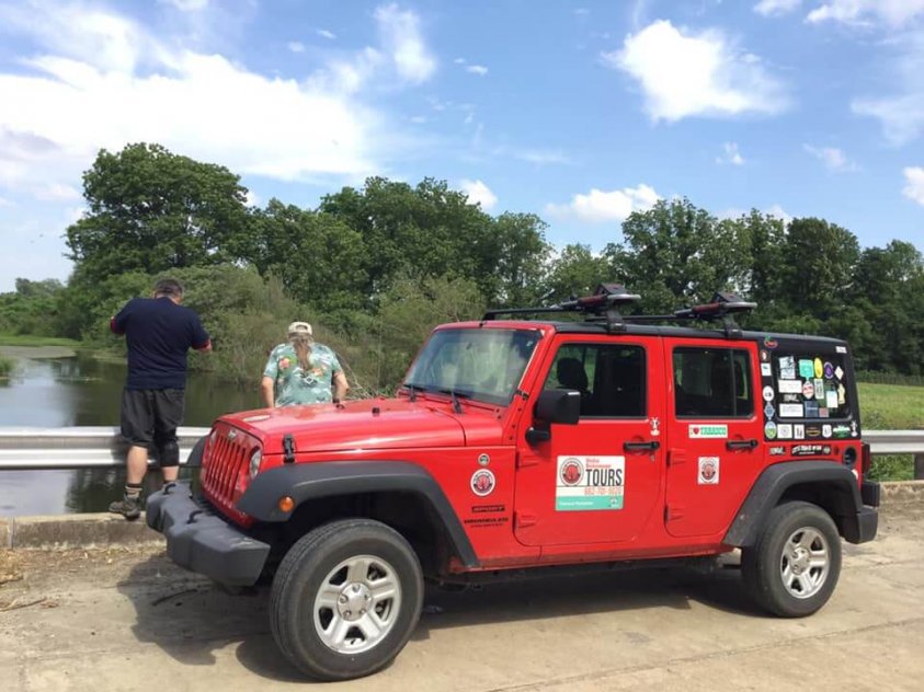 A red jeep parked in the grass near some trees.