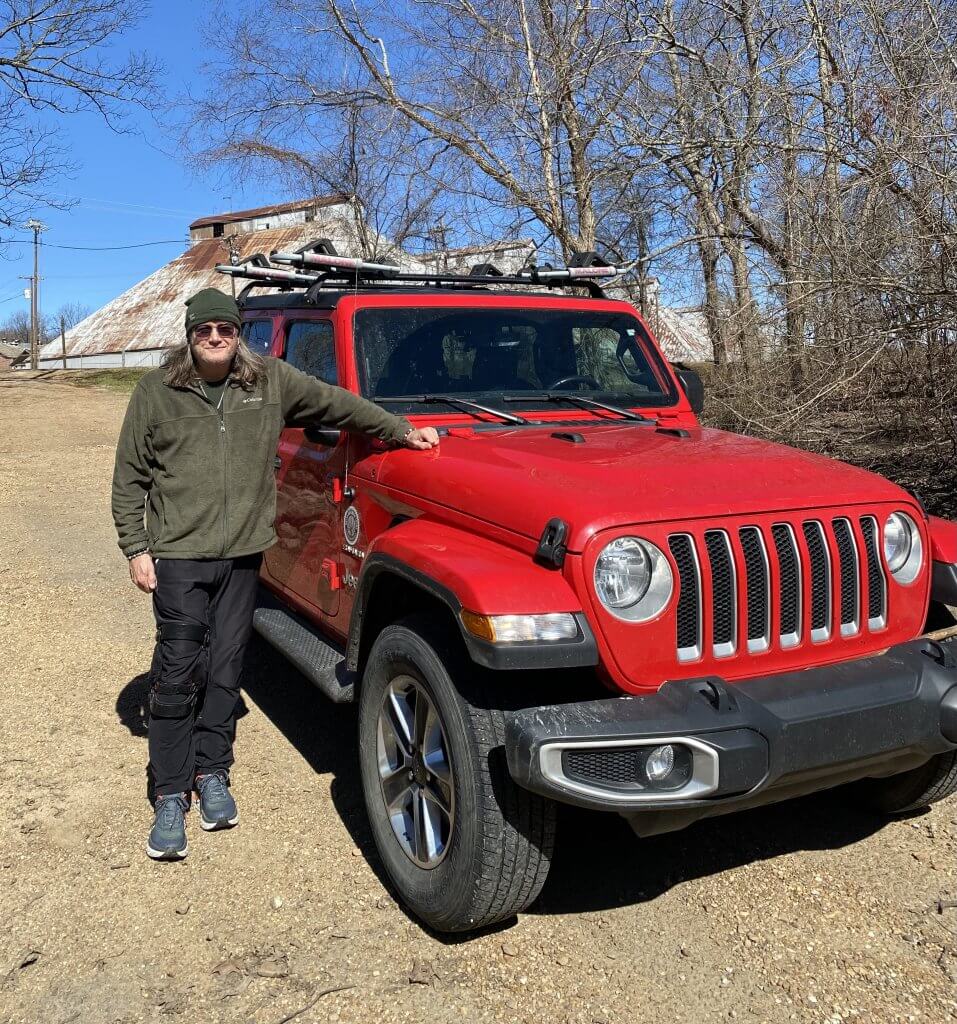 A man standing next to a red jeep.