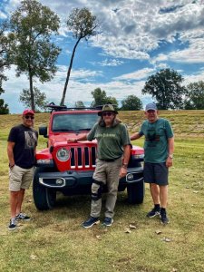 Three men standing in front of a red jeep.
