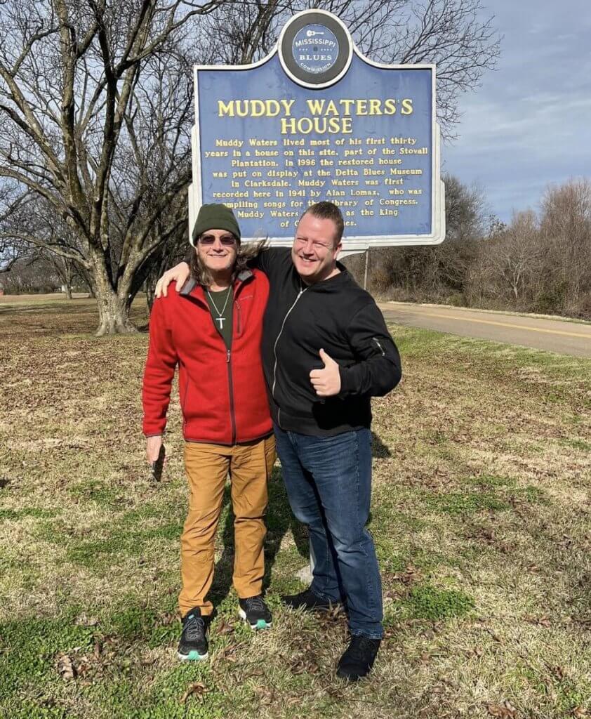 Two men standing next to a blue sign.